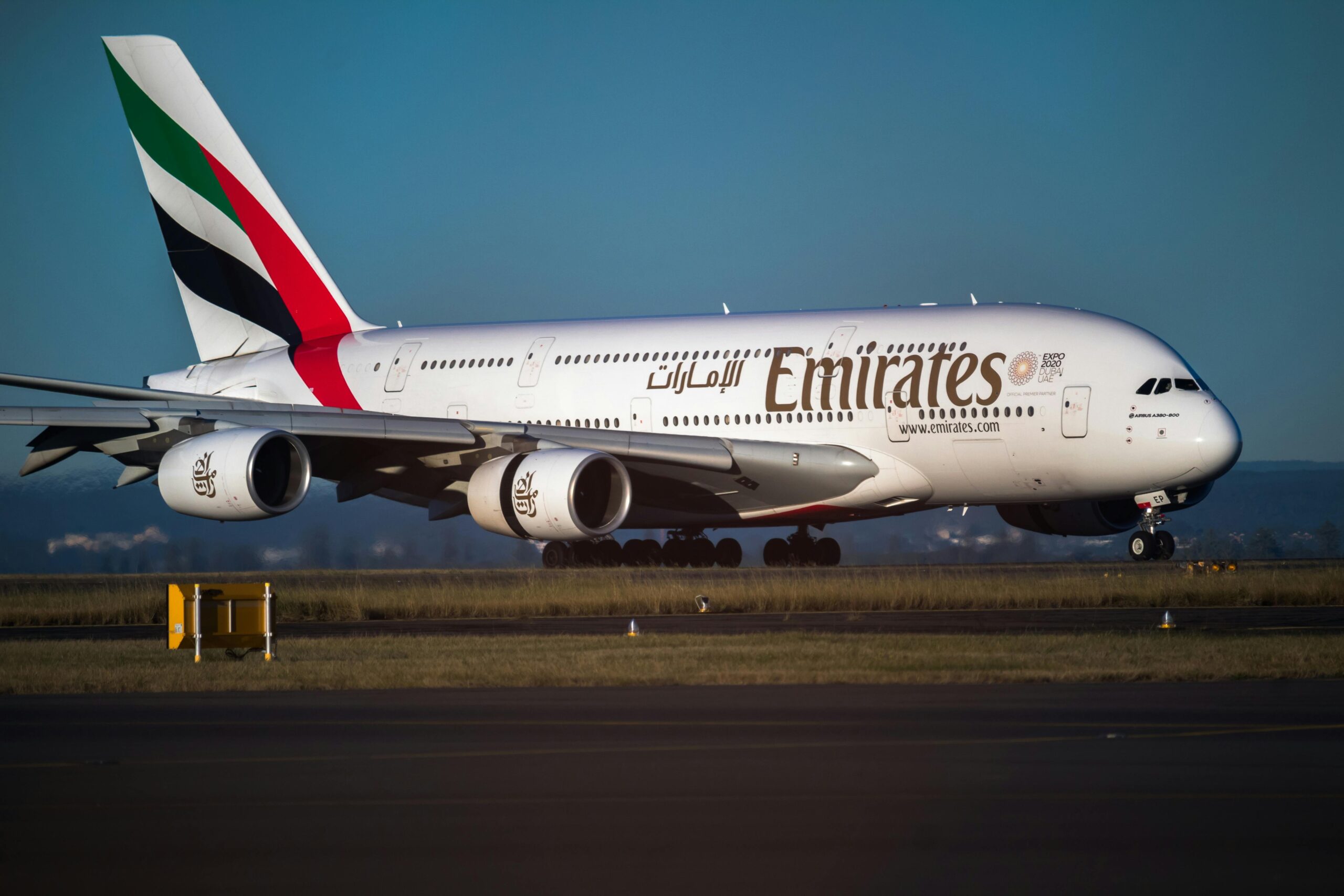 Emirates Airbus A380 aircraft on runway with clear blue sky background.